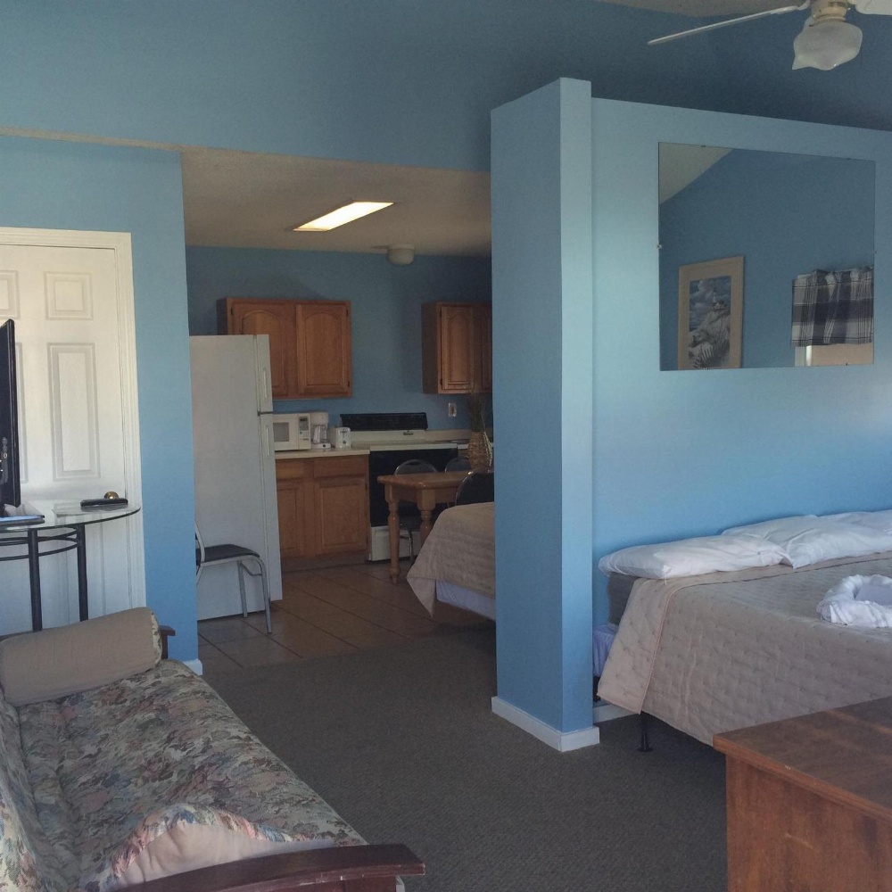 A wide view of a hotel suite with a kitchenette, sofa, bed, and mirror.