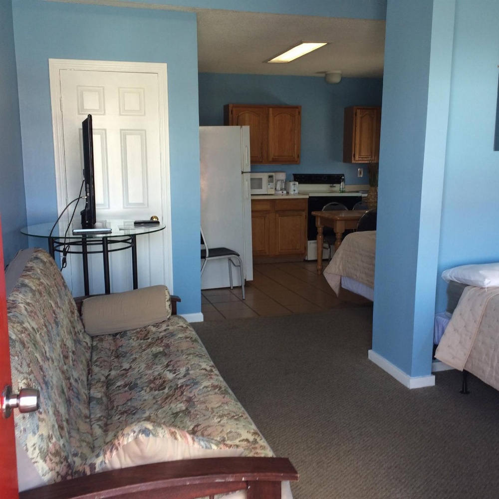 A wide view of a hotel room with a sofa, kitchenette, and bed.