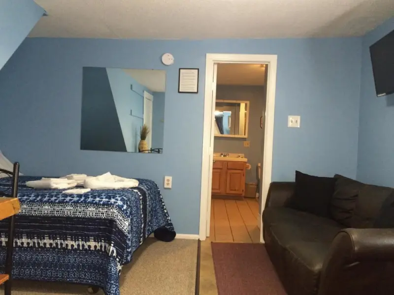 A hotel room with blue walls, a bed, a sofa, and a doorway to the bathroom.