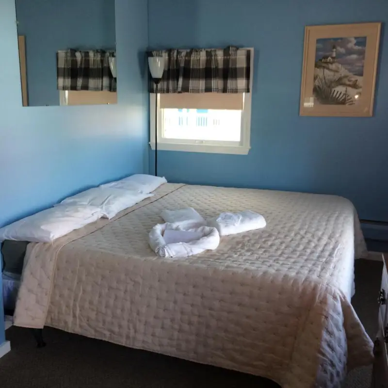 A neatly made bed in a room with blue walls, a window, and a mirror.