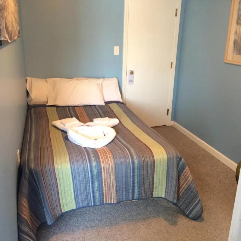 A neatly made bed with striped bedding and towels in a room with blue walls and carpeted floor.